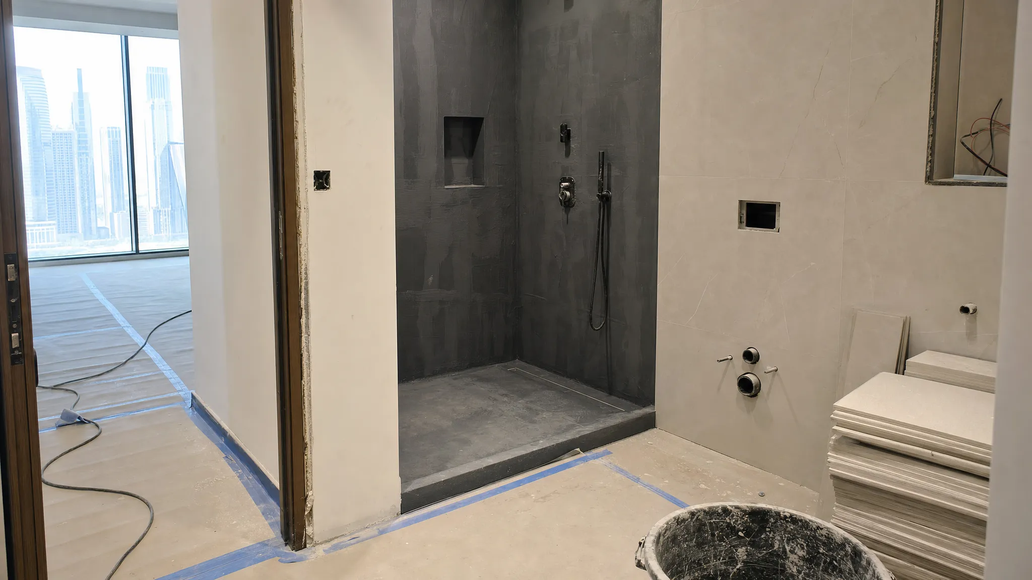 A modern Dubai bathroom renovation in progress with exposed plumbing, waterproofed shower walls, neatly stacked porcelain tiles, and covered flooring to protect the surrounding interior.