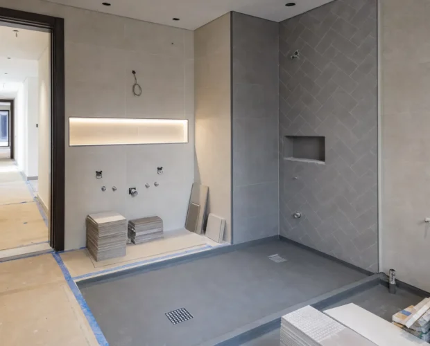 A Dubai villa bathroom under renovation shows exposed plumbing, a floor drain, tile stacks, and waterproofed surfaces ready for finishing.